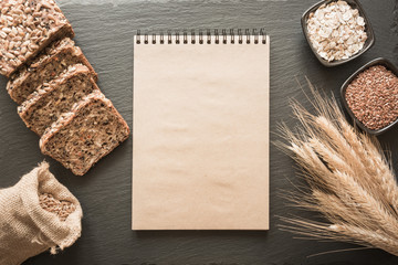 Empty blank for recipe of bread with ingredients, flour, wheat, bread, rye, flax seeds around on black slate dish. Top view and copy space.