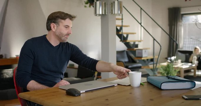 Handsome Man at Home closing Laptop, leaning back and rdrinkind a cup of coffee