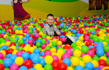 Fototapeta na wymiar Child is playing in ball pit with colorful plastic balls in children entertainment center. Pool with bright balls background. Fun, game and play of a boy.