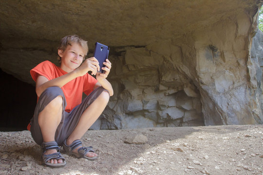 Boy hiker taking picture of mountain landscape with camera phone from natural rocky cave