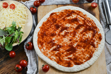 Ingredients for Pizza: basis dough, salami sausage, cherry tomatoes, grated cheese, tomato paste, herbs and arugula. Natural Wooden Background With Linen Napkin and Knife For Pizza