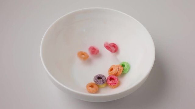 A bowl being messily filled with generic dry sugar coated fruity flavored breakfast cereal with some spilling onto a white counter top.