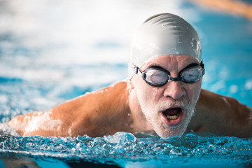 Senior man swimming in an indoor swimming pool. - Powered by Adobe
