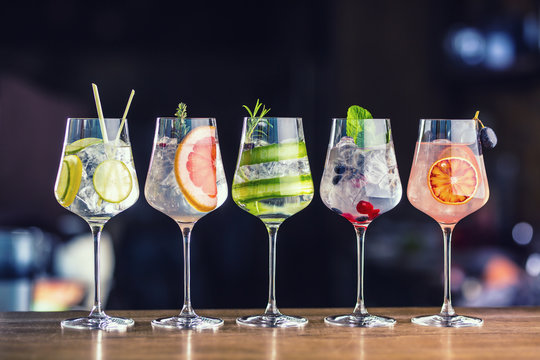 Five colorful gin tonic cocktails in wine glasses on bar counter in pup or restaurant