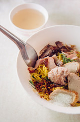 Thai egg noodle in white bowl with sliced red barbecue pork, pork ball, fish sausages vertical shot on white background