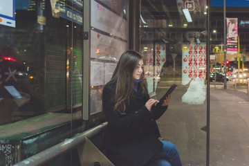 Young woman outdoor using tablet hand hold waiting bus stop - technology, social network, commuting concept