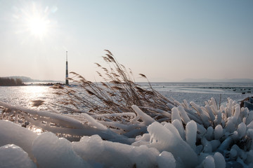 sunshine over frozen lake, light tower, port and reeds covered by ice, afternoon, Balaton, Hungary,...