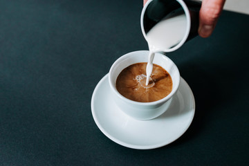 Pouring creme in cup of coffee. Close-up.