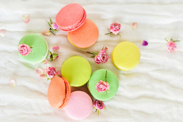 Delicate Fresh Colorful French Macaroons In Pastel Colors With Flowers Roses On A Light Textile Background, Top View