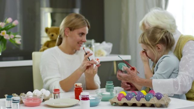 Beautiful woman talking with daughter and senior mother while painting eggs for Easter dinner