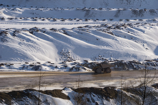 Large truck transporting ore across an open pit mine in winter