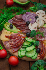 Cold smoked meat with prosciutto, salami, bacon, pork chops, cheese, mushrooms, cucumber, bread, avocado, onion and olives. Wooden rustic background. Top view
