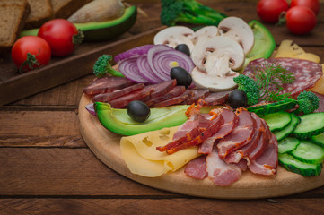 Cold smoked meat with prosciutto, salami, bacon, pork chops, cheese, mushrooms, cucumber, bread, avocado, onion and olives. Wooden rustic background. Top view