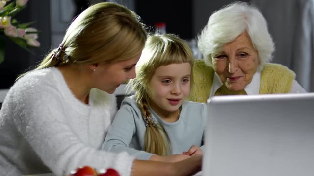 Beautiful mother, little daughter and grandmother smiling and discussing something on laptop screen
