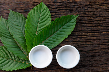 Kratom (Mitragyna speciosa) Mitragynine leaves with empty white ceramic bowls on wooden table background
