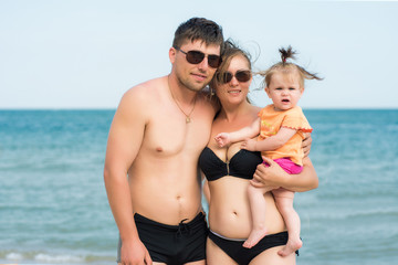 Fototapeta premium Young parents are holding a small daughter on the back of the sea and the sky
