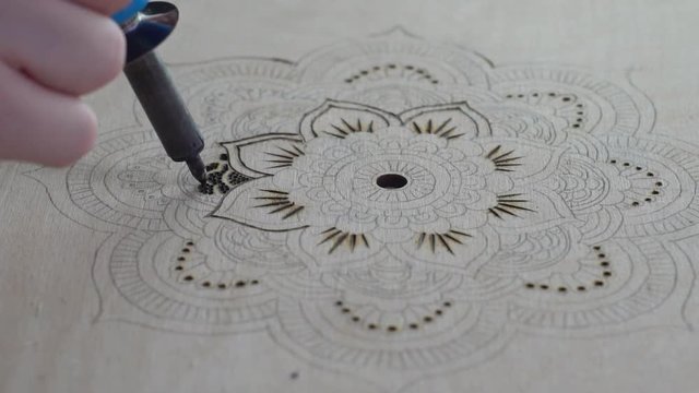 Woman making pyrography on wood, using a dot pattern