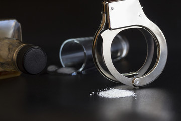 Handcuffs, whiskey, and drug on black background. Concept arrest alcohol and cocain