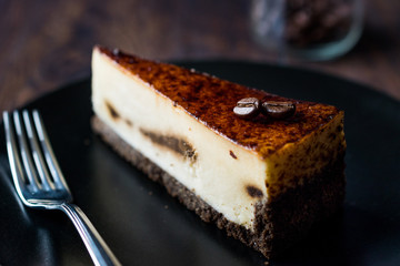 Coffee Cheesecake on Black Plate with Dark Wooden Surface.