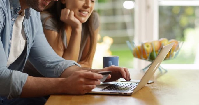 4K Happy smiling couple shopping online with credit card & pressing button to confirm their purchase. Slow motion.