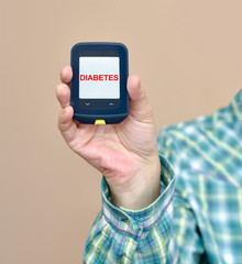Hand of a person holding and showing glucose meter. The monitor shows DIABETES. Selective focus. 