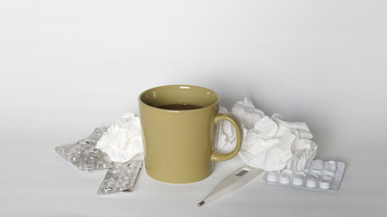 Grippe bzw. Erkältung: Tabletten-Blister, benutzte Papiertaschentücher, Fieberthermometer und eine Tasse heißer Tee