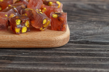 Turkish joys with different nuts are a glass of tea and a spoon. Eastern sweets. Traditional Turkish delight (Rahat lokum) on a wooden background. Side view.