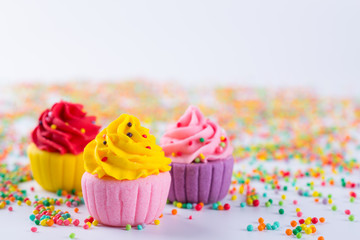 Three miniature multicolored sugar  cupcakes on light background with sprinkles
