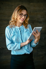 Happy attractive businesswoman using a tablet. Dressed in elegant blouse, in eyeglasses.