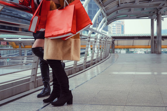 midsection two young woman holding many colorful red shopping bags together walking in modern city, winter and summer sale, promotion, mid year sale, people, payment and shopping online concept - Powered by Adobe