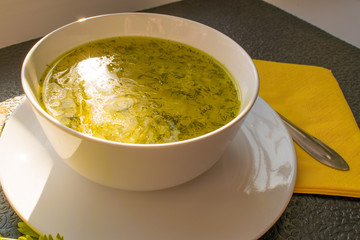 Appetizing chicken broth soup on a black table with bread and parsley