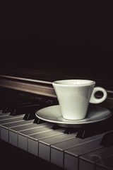 Cup of coffee on piano keys with copy space, concept of coffee break musical pause