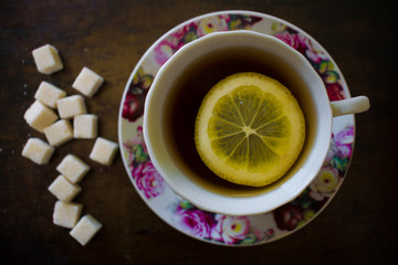 Fragrant tea with a slice of lemon in a bright pink mug, next to thirteen sugar cubes of refined sugar