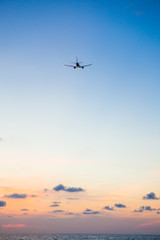 Fototapeta na wymiar Airplane flying above sea at sunset