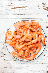 Prepared shrimps on a white plate over old white wooden table with copy space, top view
