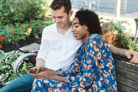 A young couple sitting on a park bench listening to music