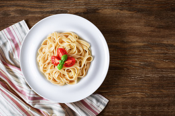 Plate with tagliatelle pasta and napkin on a wooden background.