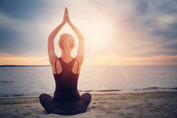 young woman sitting on the beach and practicing yoga