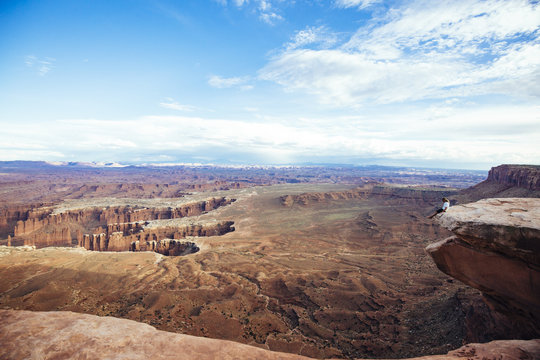 A young man dangerously sitting on the edge of a huge cliff