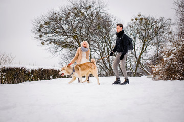 A lovely couple plays with her dog in a snowy park