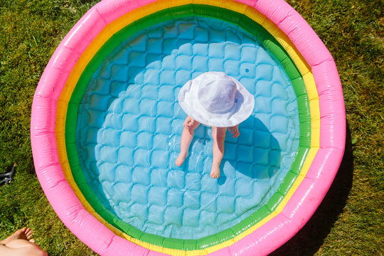 Baby Girl In Sunhat Sitting In Colorful Backyard Pool