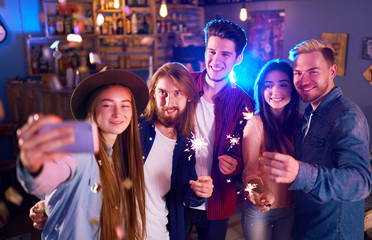 Selfie Time.Young Group of Friends Partying In A Nightclub And Toasting Drinks. Happy Young People With Sparklers At Pub. The People Have A Great Mood And They Smile A Lot.