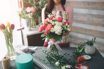 Female florist at work: pretty young dark-haired woman making fashion modern bouquet of different flowers. Women working with flowers in workshop