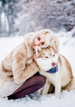 Ideal girl in a fur coat sitting with her dog in a winter forest