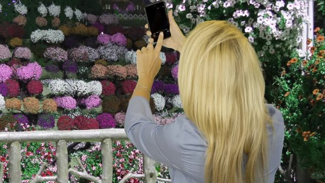 Beautiful woman making selfie photo on mobile phone in flower garden