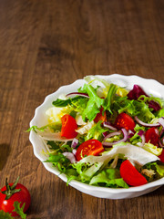 various fresh mix salad leaves with tomato in bowl on wooden background