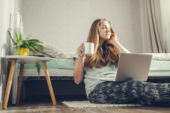 Young woman drinking coffee using her laptop in the bedroom and listening to the music