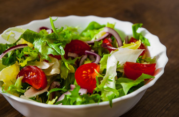 various fresh mix salad leaves with tomato in bowl on wooden background