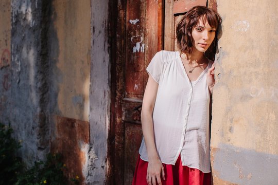 Young brunette woman in casual outfit standing near the doors of an old house