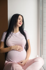 Portrait of smiling pregnant woman sit in window sill